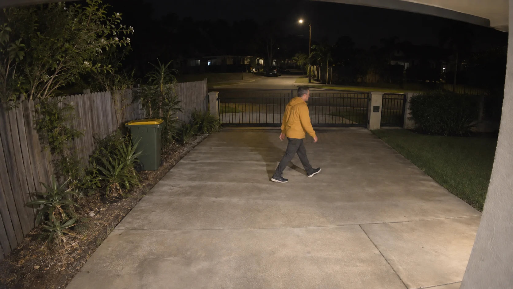 AI-generated teaching scene: a person in a mustard jacket crossing a lit driveway.